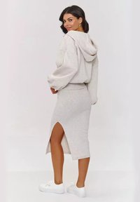 Jasnoszara bluza z kapturem o oversize'owych rękawach zestawiona z dopasowaną spódnicą midi z bocznym rozporkiem, noszona z białymi sneakerami.