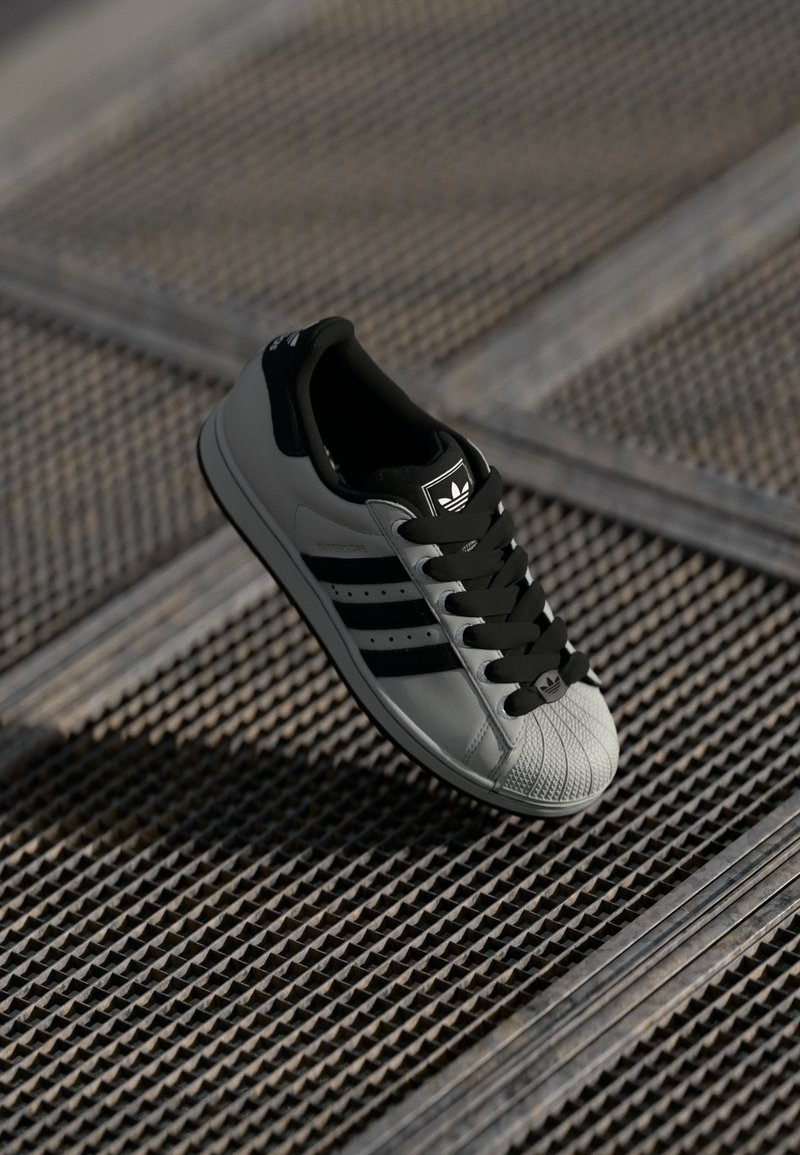 Black and grey sneaker featuring a textured rubber sole, three black stripes, and a lace-up design with a white toe cap.