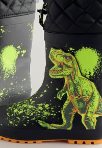 Crne gumene čizme s teksturiranim gornjim dijelom, s grafikom zelenog dinosaurusa i prskanjem; svijetla narančasta potplat za kontrast.