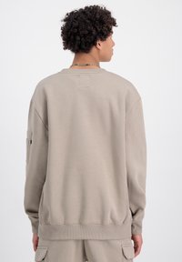 Sweatshirt beige con una vestibilità rilassata, polsini e orlo a costine. Presenta una piccola etichetta sul retro e una tasca laterale sulla manica. Tessuto liscio.