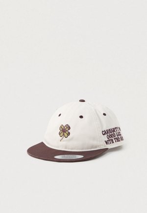 Balta un brūna snapback cepure ar izšūtu četru lapu āboliņu un tekstu "Carhartt WIP Good Luck With The Run" uz sānu paneļa.