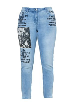 Lyseblå jeans med sort trykt motiverende tekst på lommerne og låret, med et monokromt grafisk patch på venstre ben.