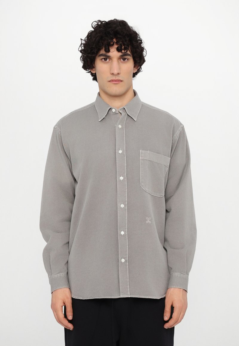 Chemise grise à manches longues en tissu doux, avec un col à boutons, une poche avant et de subtils détails de couture.