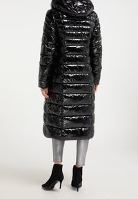 Černá prošívaná bunda s lesklým povrchem, dlouhým střihem, vodorovným prošíváním a kapucí. Spojená s metalickými stříbrnými legínami a černými kotníkovými botami.