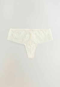String en dentelle écru avec broderie florale à la taille, présentant des bords ondulés et un dos lisse.