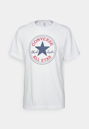 T-shirt bianca in cotone con una grafica circolare che presenta una stella blu, la scritta rossa "CONVERSE" e il testo "Chuck Taylor ALL STAR". Maniche corte, vestibilità casual.