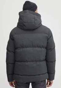 Puffer jacket in dark gray with a high collar and hood. Features horizontal stitched sections, a matte finish, and a relaxed fit.