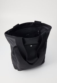 Black tote bag with a smooth, matte texture. Features two sturdy handles, an interior zip pocket, and a front pocket with a snap closure.