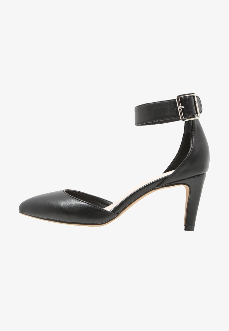 Chaussure à talon haut en cuir noir à bout pointu, avec bride à la cheville et boucle argentée, talon fin de hauteur moyenne, vue de profil.