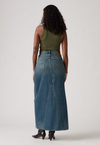 Denim maxi skjørt i blått med en tettsittende midje, to baklommer og splittdetalj. Brukt med en grønn tanktop og svarte hæl støvler.