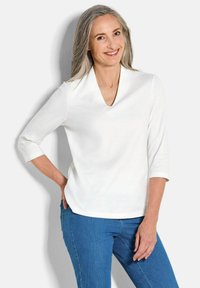 Witte V-hals top met driekwart mouwen, gemaakt van een soepele stof. Gedragen met blauwe jeans, die een ontspannen pasvorm en minimalistisch ontwerp laten zien.
