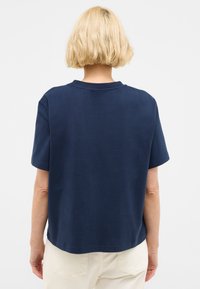 T-shirt en coton bleu marine à manches courtes et col rond, avec une coupe ample et une texture unie, porté avec un pantalon de couleur claire.