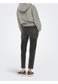 Bluza z kapturem z bawełnianego sztruksu w stonowanej zieleni, z elastycznym pasem, w połączeniu z szarymi, dopasowanymi dżinsami, posiadającymi dwie tylne kieszenie, oraz klasycznymi trampkami.