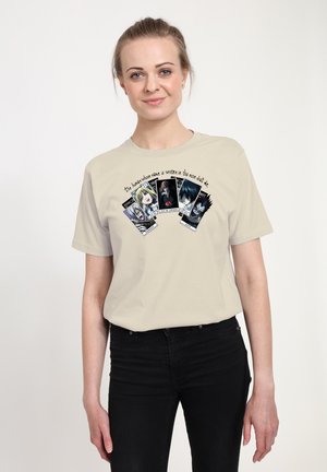 T-shirt en coton beige présentant cinq cartes illustrées avec des personnages et du texte, sur fond uni. Manches courtes et coupe décontractée.