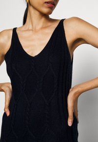 Robe tricotée marine avec un col en V, sans manches, texture côtelée et motifs en losange intégrés dans le tissu.