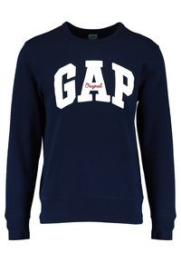 Sweat-shirt bleu marine à manches longues avec lettres blanches "GAP" et texte rouge "Original" centré sur le devant.