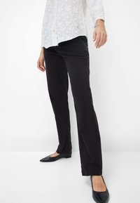 Schwarze, gerade geschnittene Hose aus Baumwollmix, kombiniert mit schwarzen, spitz zulaufenden Ballerinas. Weiße, bestickte Bluse mit floralem Muster.