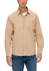 Beige Langarmhemd mit Knopfleiste, aus Baumwolle, mit einer Brusttasche, klassischem Kragen und entspanntem Schnitt. Getragen mit blauen Jeans.