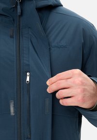 Giacca blu navy con zip frontale, dettagli in Velcro e logo. Realizzata in materiale liscio e impermeabile, adatta per l'uso all'aperto.