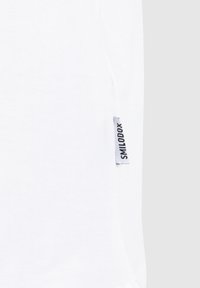 Weißes Baumwoll-T-Shirt mit einer glatten Textur und einem kleinen grauen Etikett mit "SMILODOX" an der Seitennaht. Einfaches und minimalistisches Design.