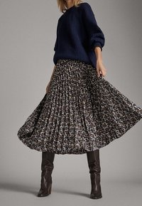 Marine gebreide trui gecombineerd met een lange, geplooide rok met luipaardprint. Bruine laarzen tot de knie maken de outfit compleet en benadrukken textuur en patroon.