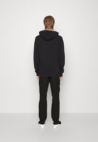 Zwarte hoodie met geribbelde manchetten en onderrand, gecombineerd met donkere cargo-broeken en witte sneakers, gezien vanachter.