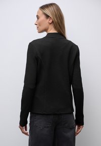 Getexturede zwarte jas met een slim-fit ontwerp, lange mouwen en een rechte zoom. Het materiaal lijkt lichtgewicht en gestructureerd.
