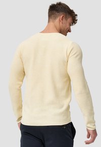 Heller, gelber Pullover mit langen Ärmeln und einem strukturierten Strickdesign, rundem Ausschnitt und schmalen Ärmeln. Nahtdetails auf der Rückseite.