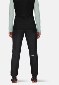 Svarta träningsbyxor med reflexdetaljer, kombinerade med en figurnära svart topp med långa ärmar i ljus mynta. Materialet är slätt och stretchigt.
