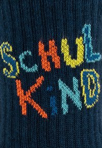 Dzianina w kolorze ciemnoniebieskim z wyrazem "Schulkind" w jasnych, wielokolorowych literach: pomarańczowej, żółtej, jasnoniebieskiej i zielonej.