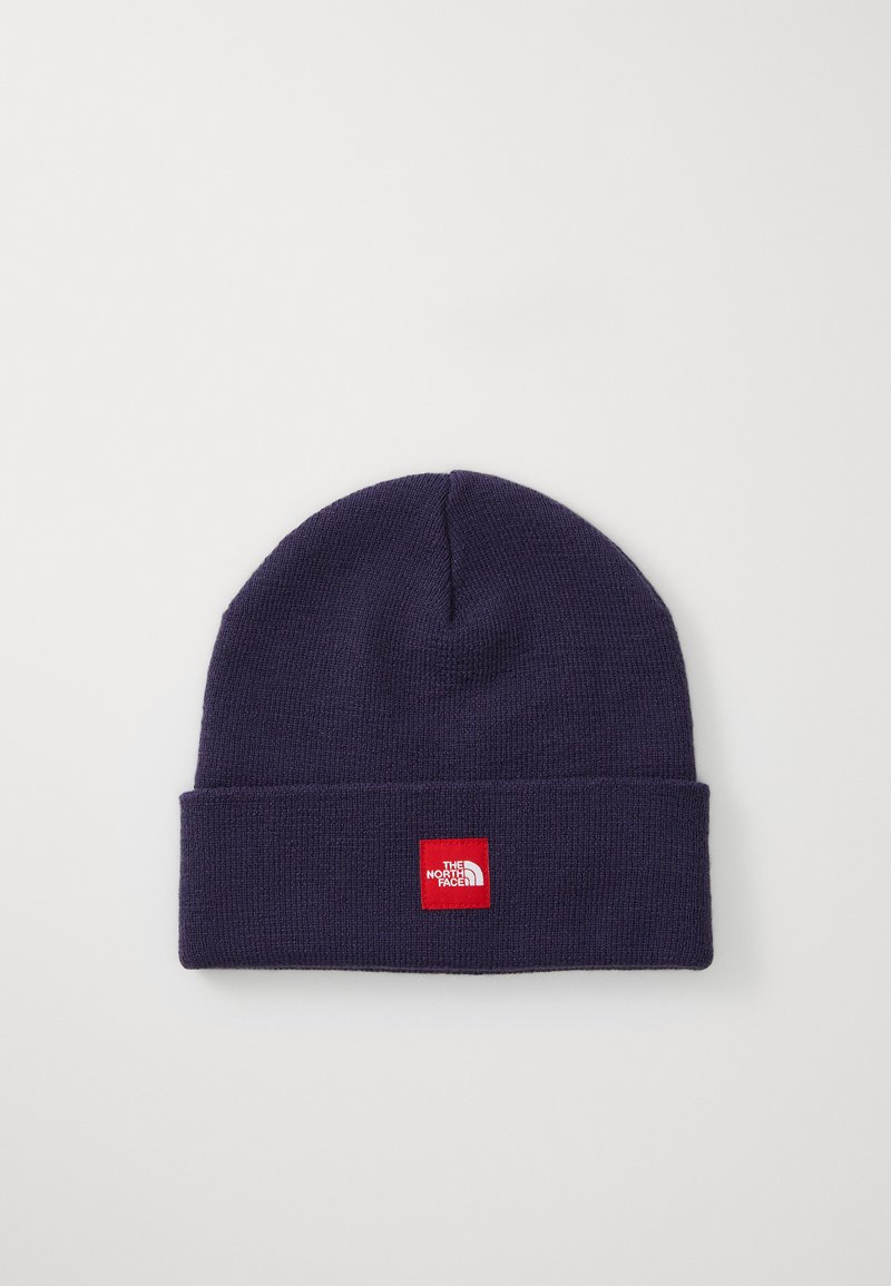 Beanie in maglia blu navy con risvolto e etichetta quadrata rossa con testo bianco. Texture morbida con design senza cuciture.