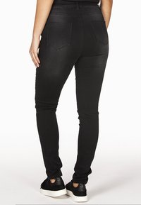 Sorte skinny jeans med høj talje, der har en glat tekstur, to baglommer og et tætsiddende bendesign. Bæres med sorte sneakers.