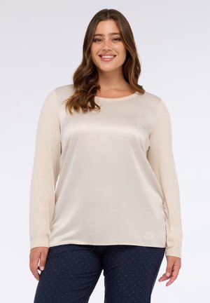 Top de manga larga en material satinado de color beige claro con cuello redondo, combinado con pantalones oscuros azul marino con lunares blancos.