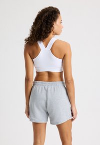 Sujetador deportivo blanco y pantalones cortos grises. El sujetador presenta un diseño de espalda racer. Los pantalones cortos tienen una cinturilla elástica y un tejido suave y texturizado.