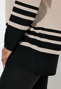 Béžový a černý pruhovaný svetr s dlouhými rukávy, svislé pruhy a boční rozparky na spodním okraji. Vyrobený z měkkého pleteného materiálu.