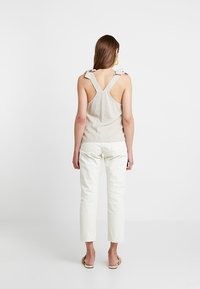 Helles beige Leinen-Top mit breiten Trägern und V-Ausschnitt, kombiniert mit weißen, cropped Hosen. Einfaches Design ohne sichtbare Muster oder Verzierungen.