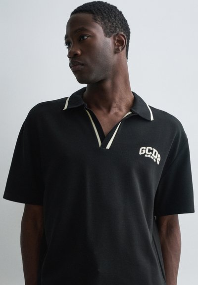 Schwarzes Poloshirt mit kontrastierendem cremefarbenem Kragen, kurzen Ärmeln und gesticktem "GCDS"-Logo auf der linken Brust. Weiches Baumwollmaterial.