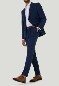 Marineblauer Anzug mit einem schlanken Jackett und Hose, ergänzt durch ein weißes Hemd und braune Leder Schuhe mit doppeltem Monk-Strap-Design.