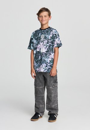 T-shirt grafico a maniche corte in nero con motivi astratti colorati; abbinato a pantaloni cargo grigi con molteplici tasche e una vestibilità ampia.