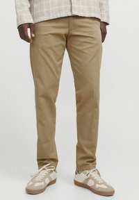 Beige cotton chinos with a slim fit, featuring side pockets and a smooth texture, paired with beige and gray sneakers.