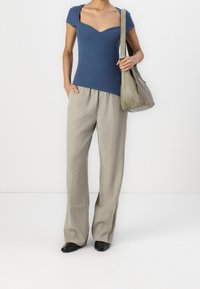Hladký modrý top s výstřihem do srdce, kombinovaný s světlými béžovými kalhotami s širokými nohavicemi a černými nazouvacími botami, s šedou kabelkou.