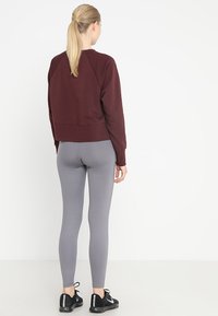 Sudadera corta burdeos y leggings grises. La sudadera tiene un dobladillo y puños acanalados; los leggings están hechos de un tejido elástico. Se llevan zapatillas negras.