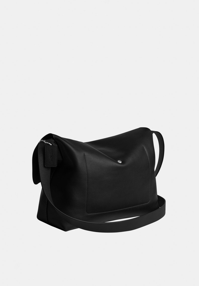 Zwarte leren schoudertas met voorvak, zilverkleurige drukknop en verstelbare riem op effen lichte achtergrond.