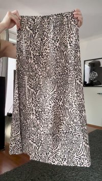 Hands holding a knee-length skirt with black and beige animal print pattern in a bright, modern living room.