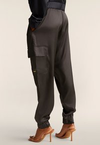 Pantaloni cargo in satin grigio scuro con tasche laterali, polsini elasticizzati e una texture liscia. Abbinati a sandali trasparenti con tacco alto.