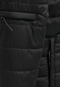 Svart puffjacka med horisontellt quiltat mönster, dragsnoddjusteringar och slät textur med en elegant finish.