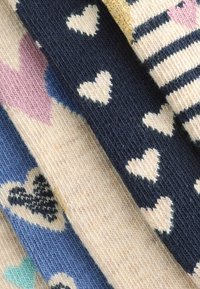 Muestras de tela de punto con varios patrones de corazones en colores: rosa pálido, azul marino, azul claro, crema y rayas doradas. Textura suave.
