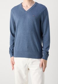 Maglione blu a V in morbido tessuto, con maniche lunghe e polsini a costine. Piccolo logo sul petto. Abbinabile a pantaloni chiari.