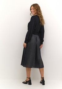 Svart långärmad blus matchad med en plisserad silverkjol, med en glansig och strukturerad tyg. Svarta klackskor avslutar looken.