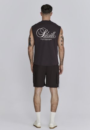 Dark sleeveless shirt with white graphic text on the back, paired with black shorts featuring side pockets. Model wearing white socks and shoes.